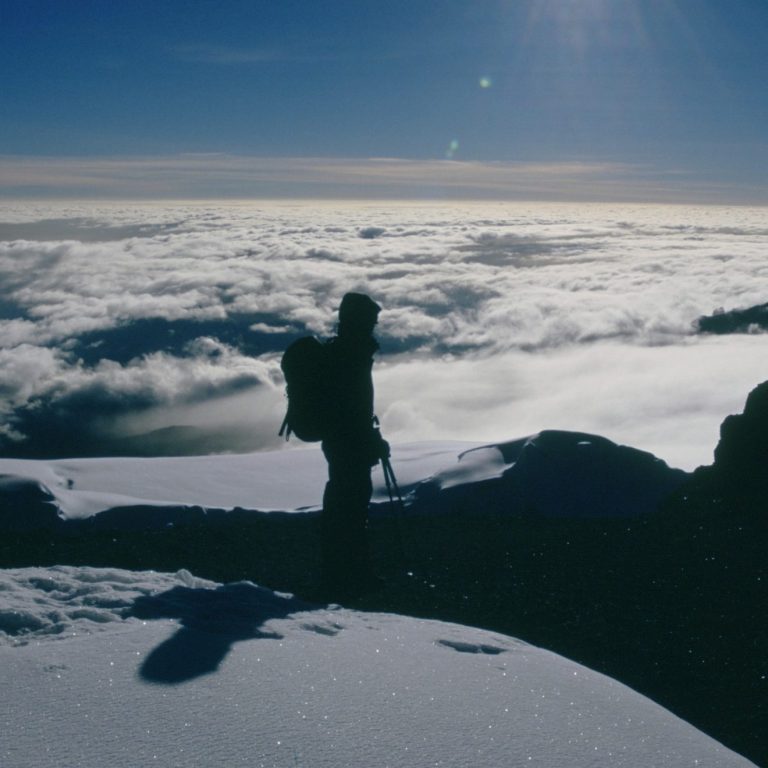 Person steht in schneebedeckter Landschaft mit Blick über Wolkenmassen.
