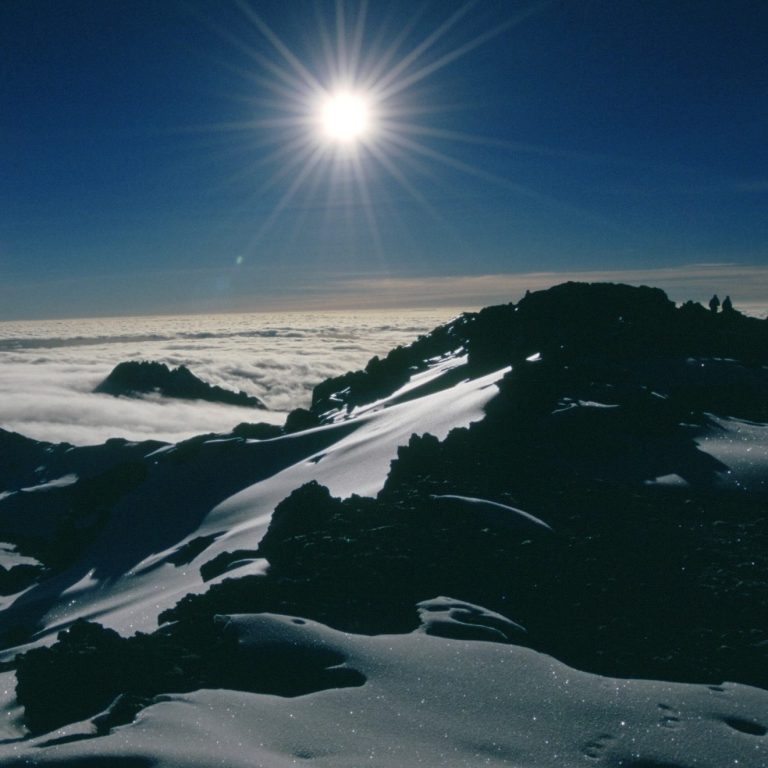 Schneebedeckte Berglandschaft mit strahlender Sonne über den Wolken.