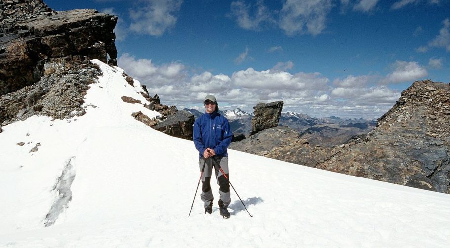 Ein Wanderer steht auf schneebedecktem Boden in einer bergigen Landschaft.