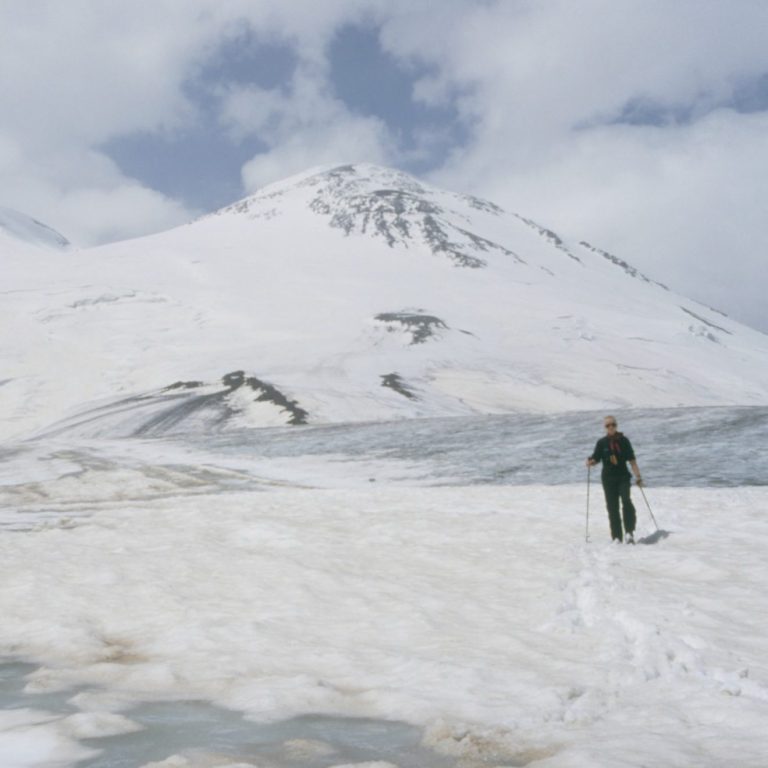 Ein Skifahrer auf einer schneebedeckten Landschaft mit Bergen im Hintergrund.
